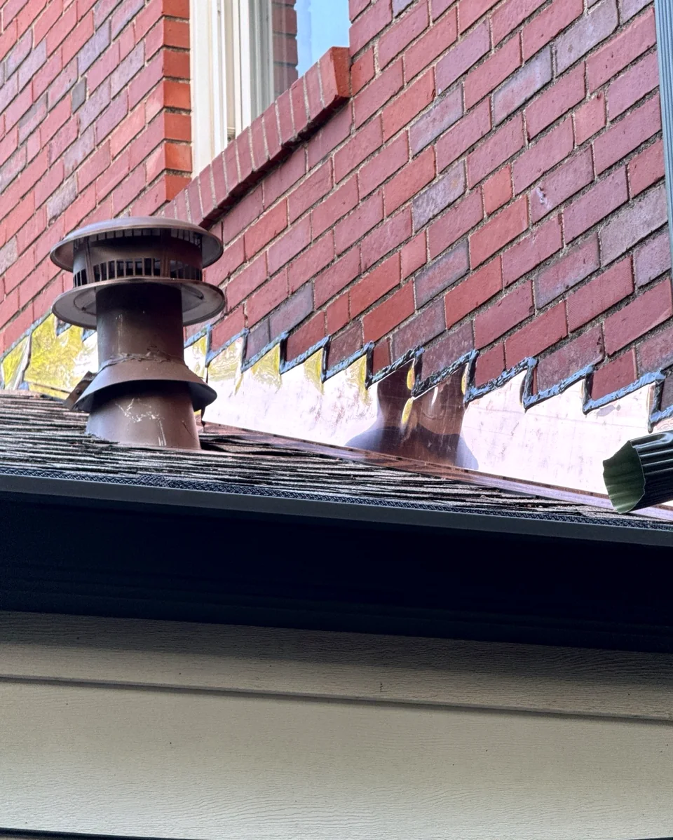 Custom copper flashing at the intersection of a brick wall and shingled roof.