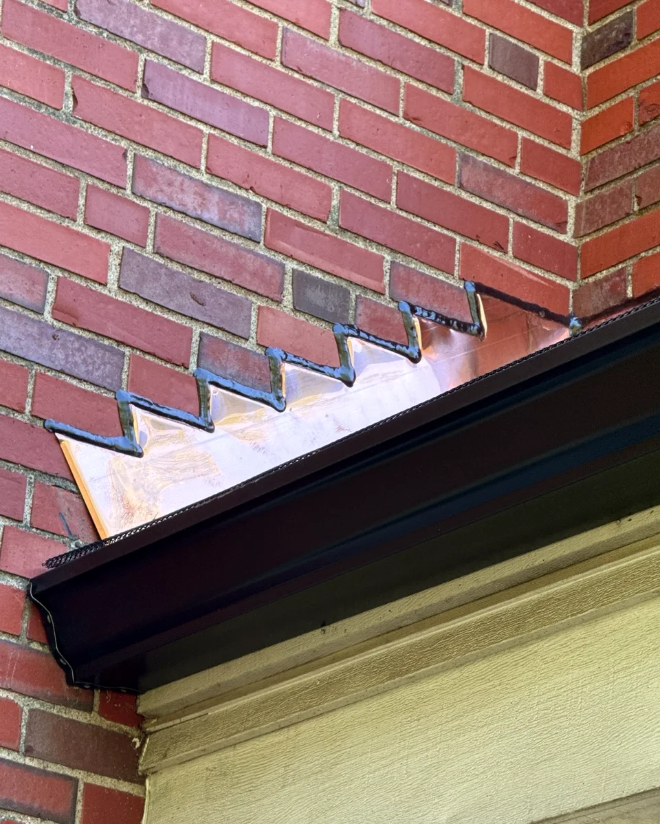 Close-up of copper step flashing where a brick wall meets the lower roof.