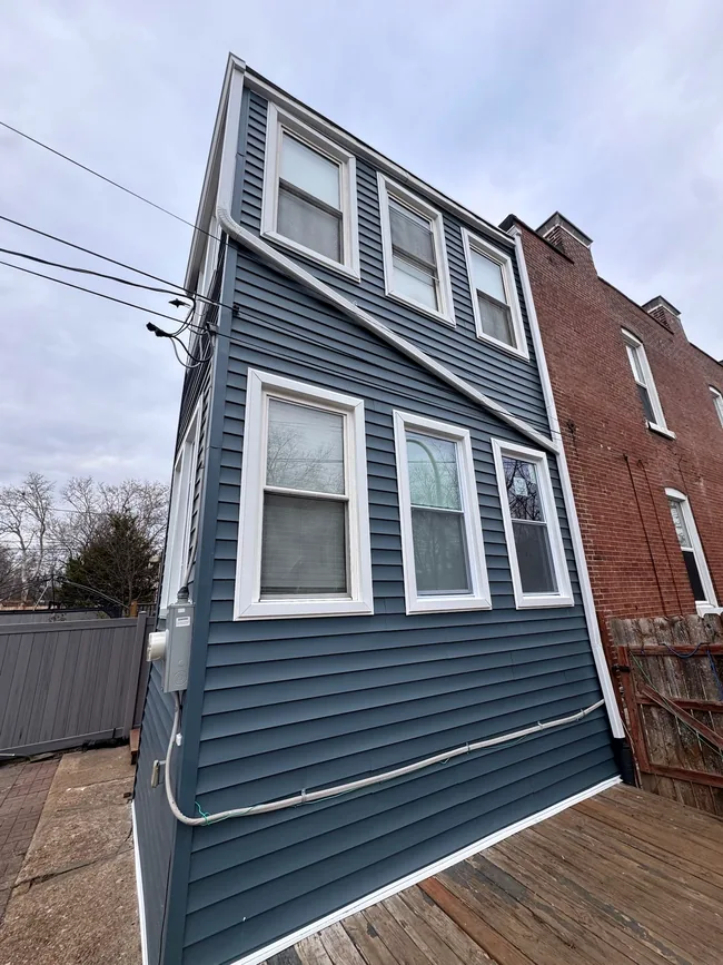 Finished blue-gray vinyl siding with white window trim on the restored St. Louis home.