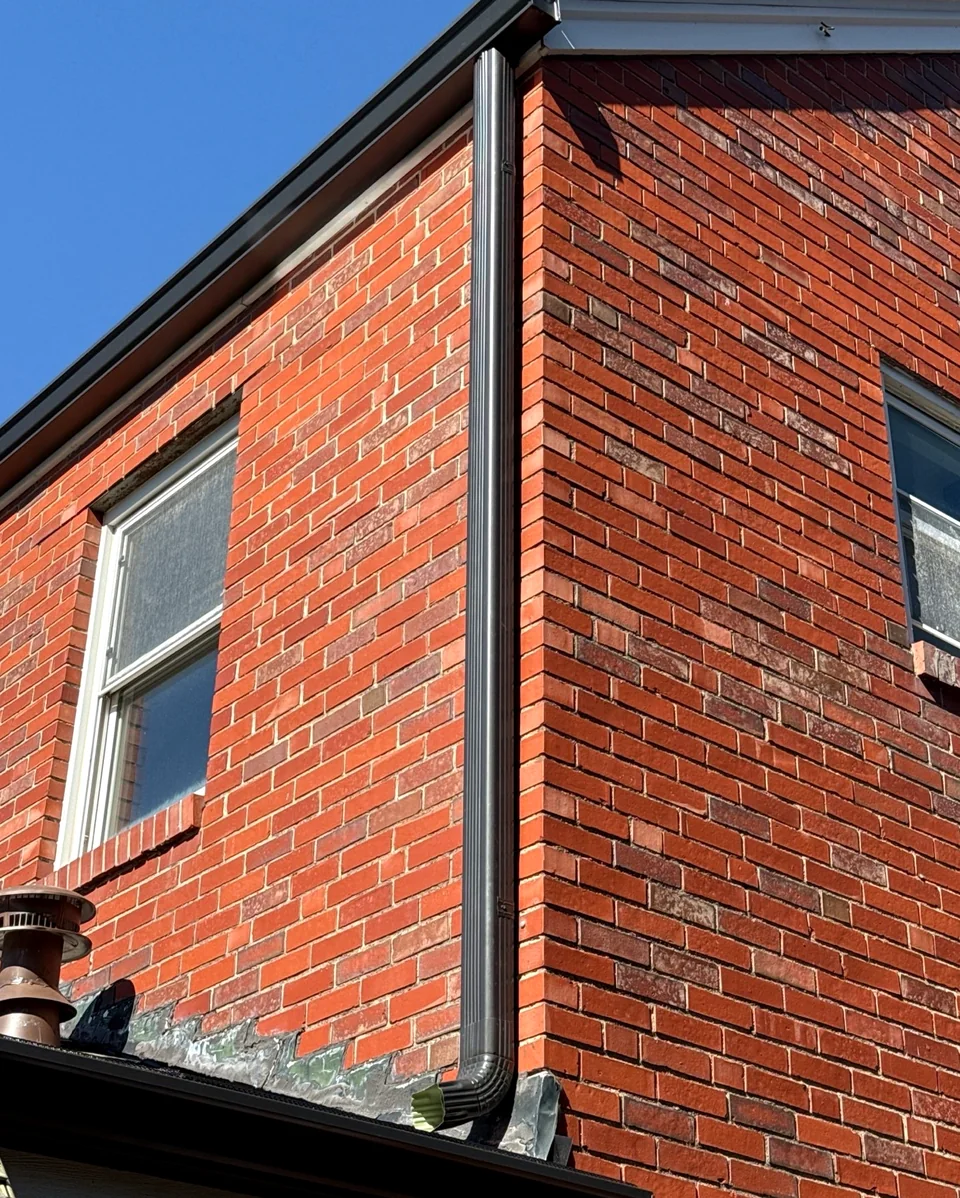 New dark metal gutter and downspout along the corner of a red brick St. Louis home.