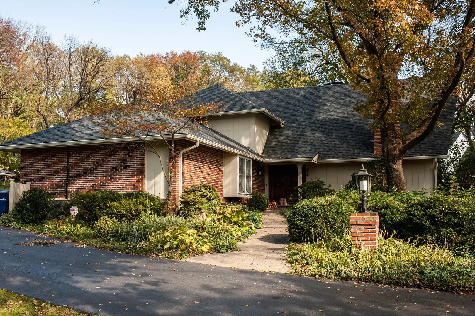 Shingle roof above a brick-and-light-sided home, with a front walkway and surrounding trees