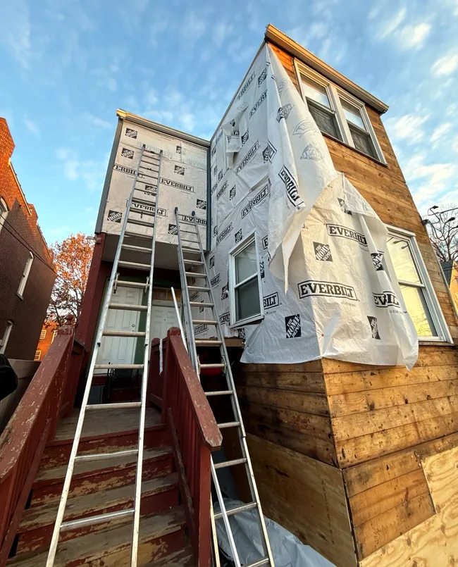 Workers installing a weather-resistant barrier around windows before new siding.